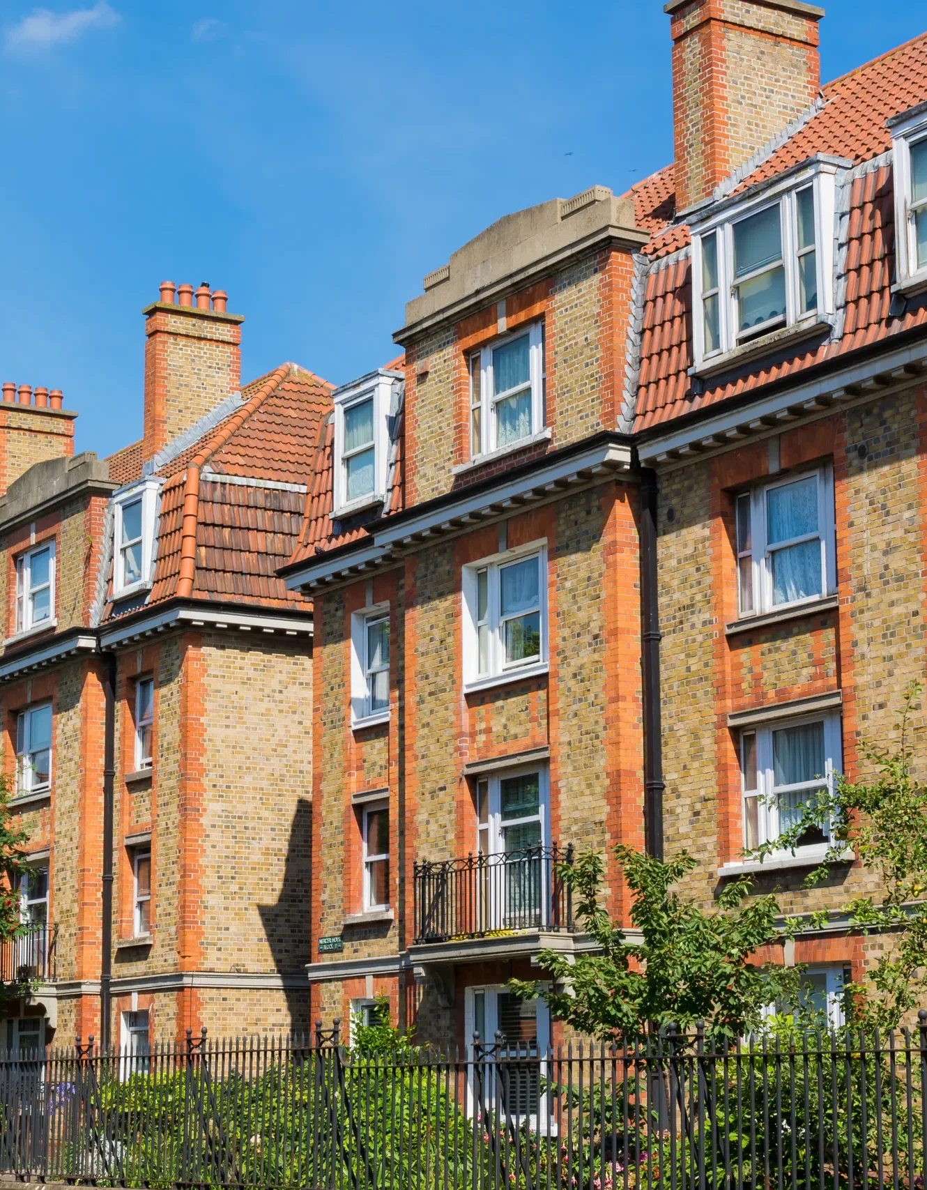 Historic brick apartment building with red-tiled roof under clear blue sky in urban setting.