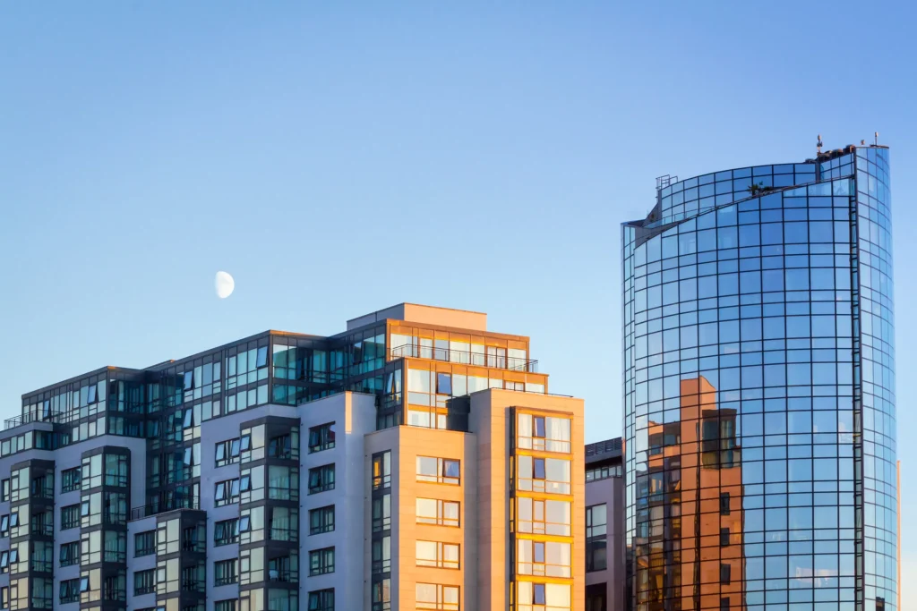 Modern glass buildings against a clear sky with a visible moon.