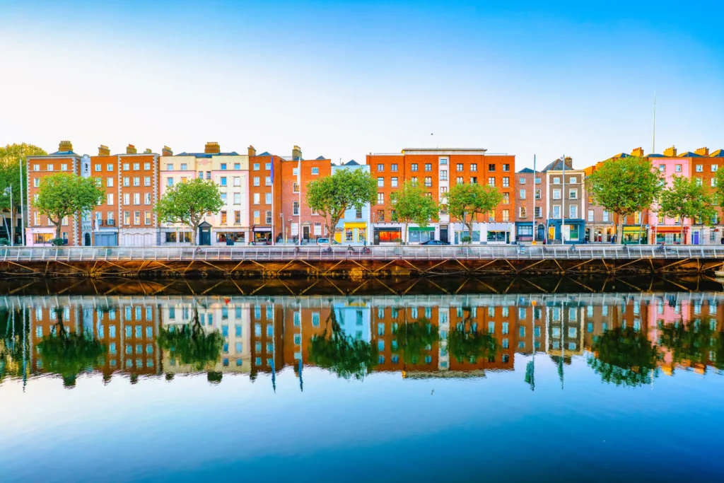 Colorful Dublin waterfront buildings reflected in the River Liffey under a clear blue sky.