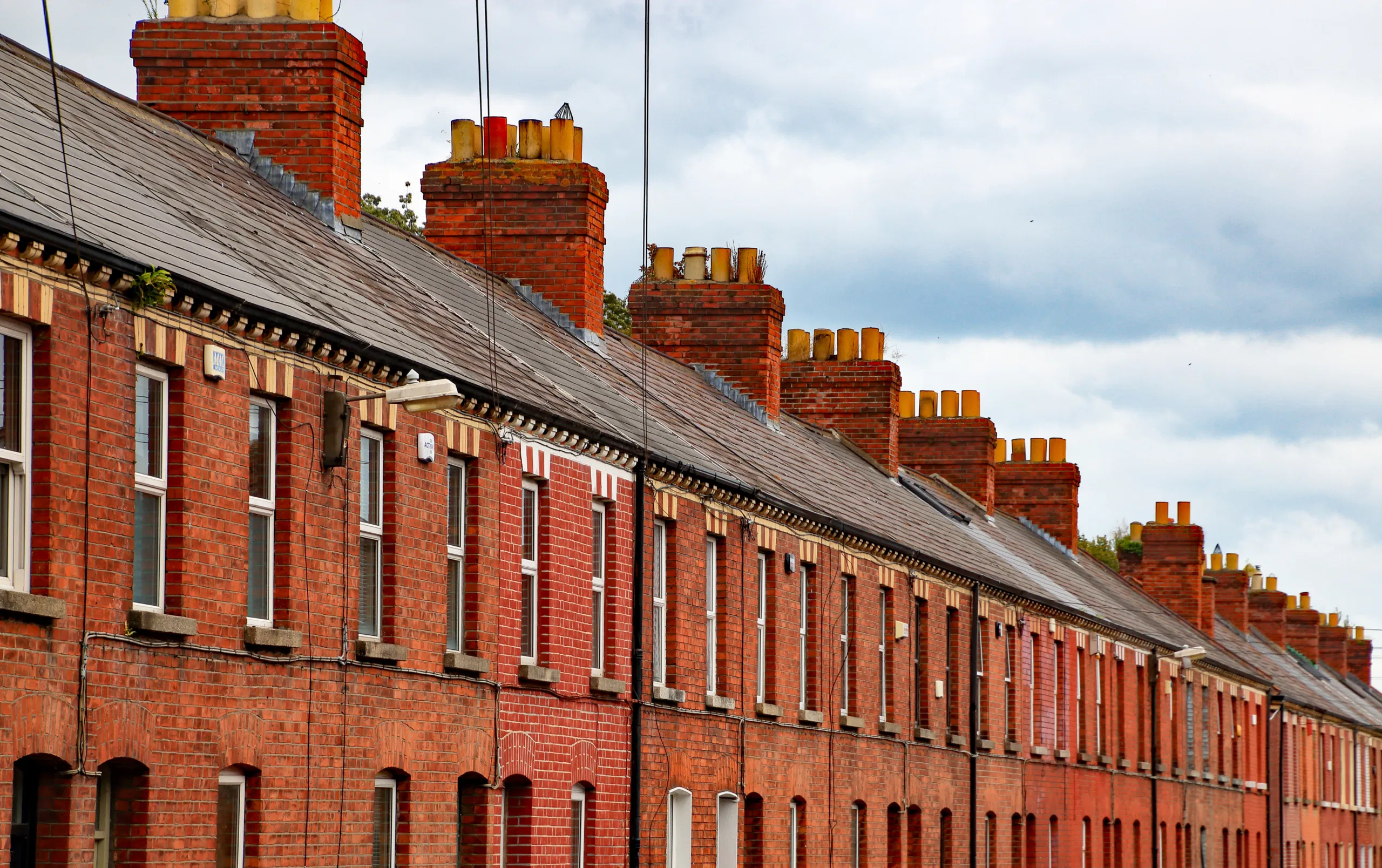 Row of traditional red brick terrace houses with chimneys under a cloudy sky.
