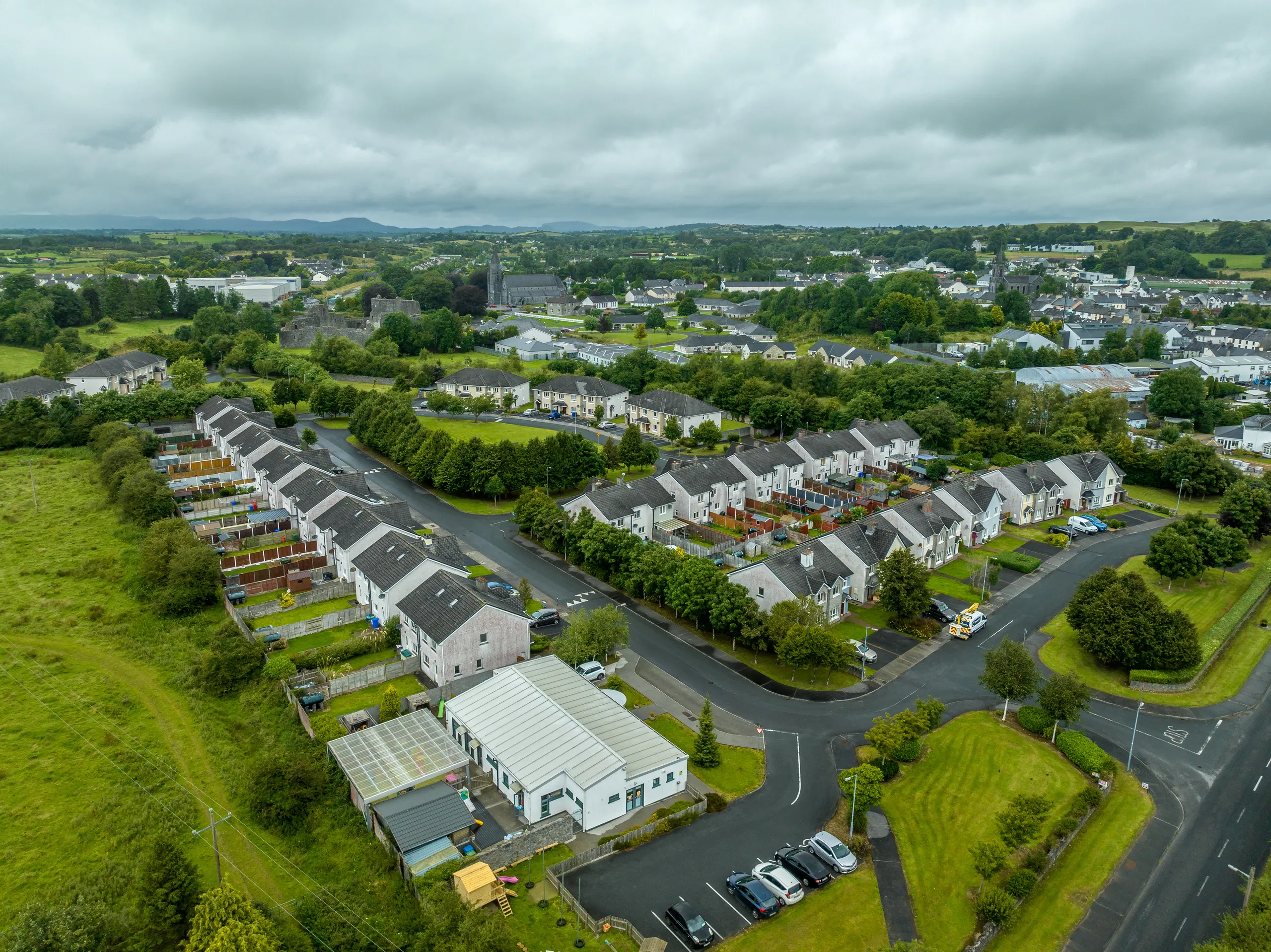 Aerial view of a residential neighborhood with green landscape, roads, and houses under cloudy skies.