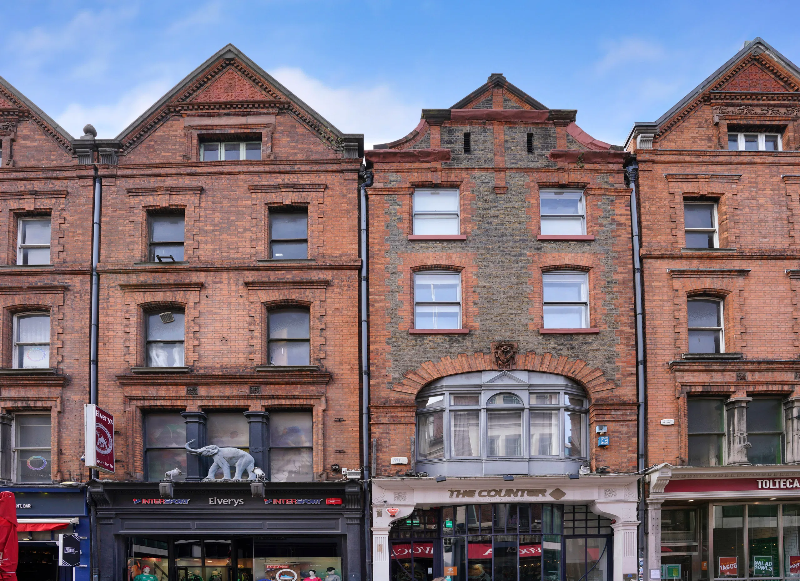 Historic brick buildings with retail shops on a street, featuring Elverys sports store with an elephant statue.