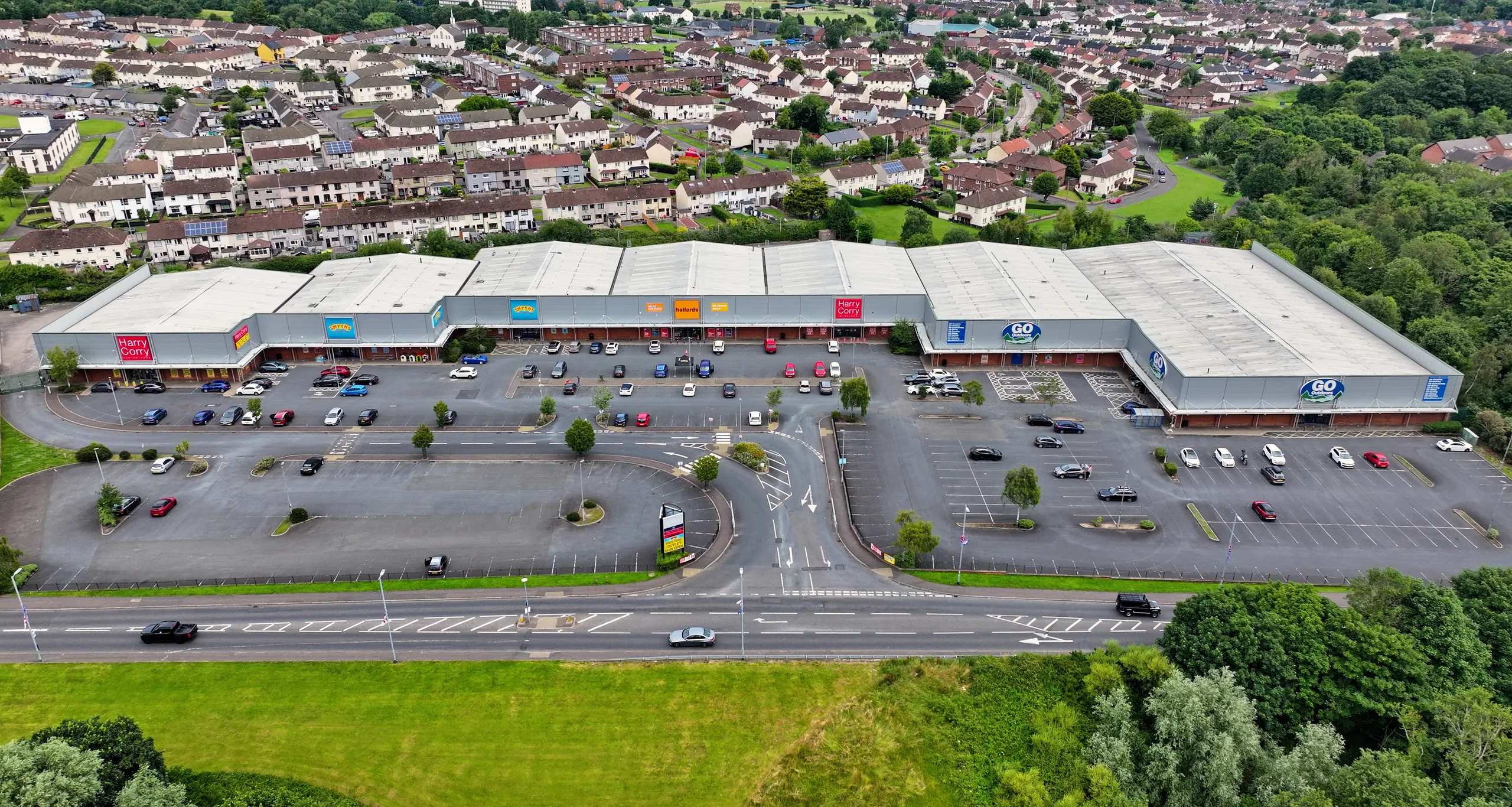 Aerial view of a retail park with parking and nearby residential neighborhood.
