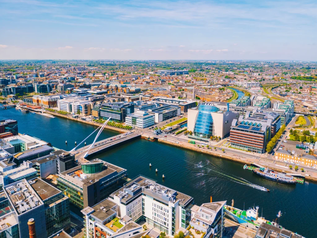 Aerial view of modern Dublin cityscape with iconic buildings and river under a clear blue sky.