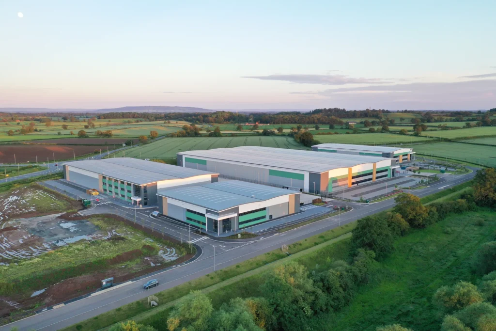 Aerial view of modern industrial facility surrounded by lush green fields at sunset.
