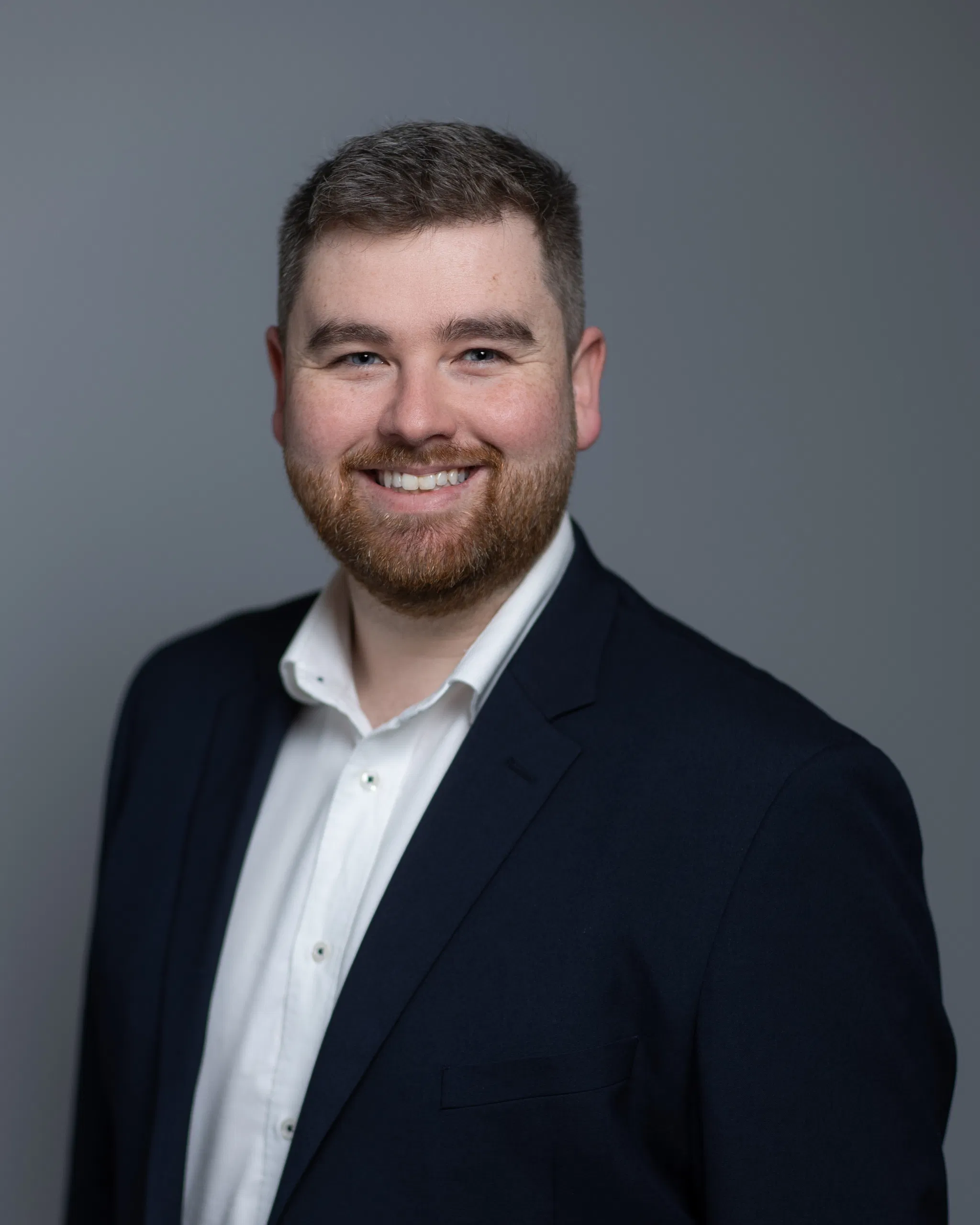 Smiling man in a suit with a gray background, professional headshot.