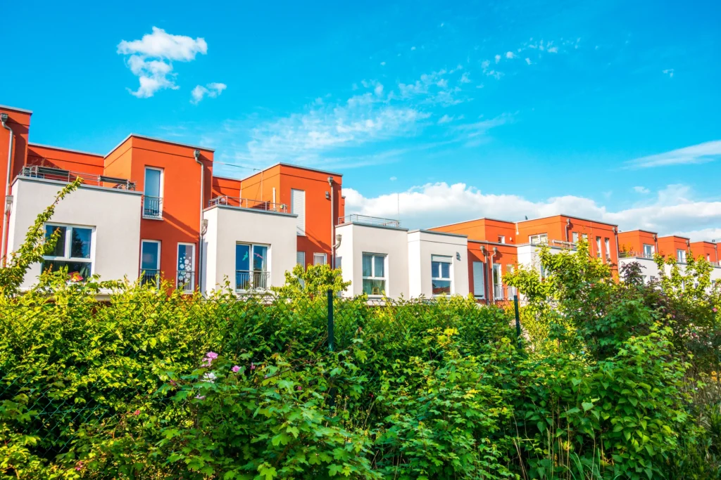 Modern townhouses with orange facades and greenery under a bright blue sky.