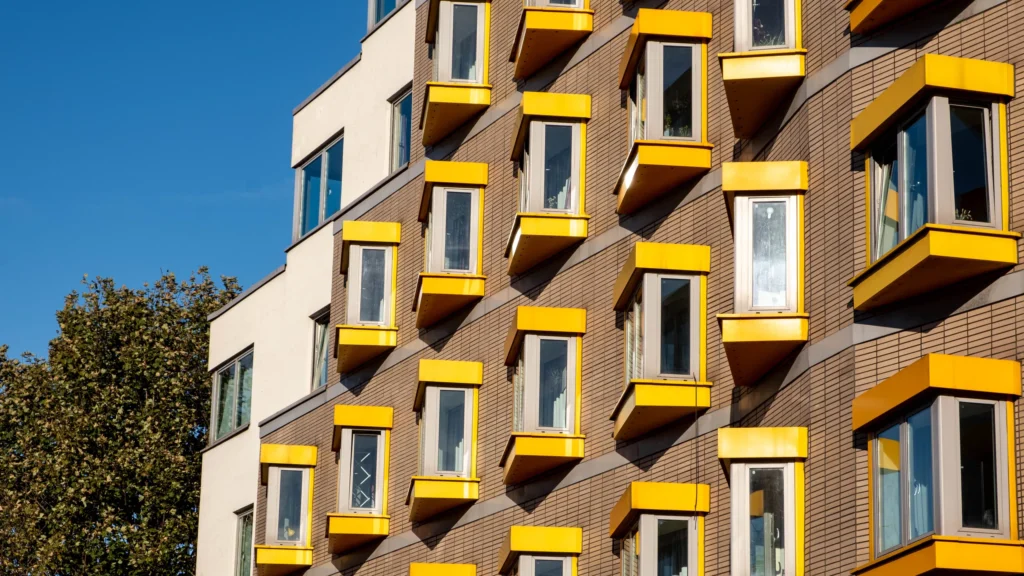 Modern building facade with vibrant yellow window frames against a clear blue sky.