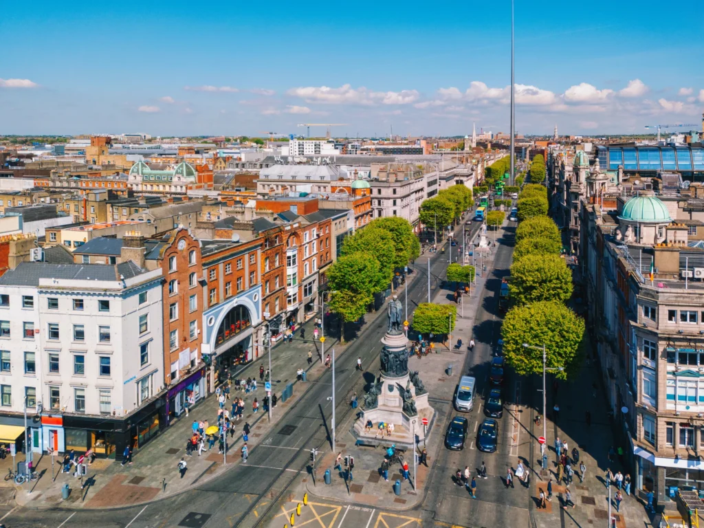 Aerial view of Dublin city center with historic buildings, green trees, and bustling streets under a clear blue sky.