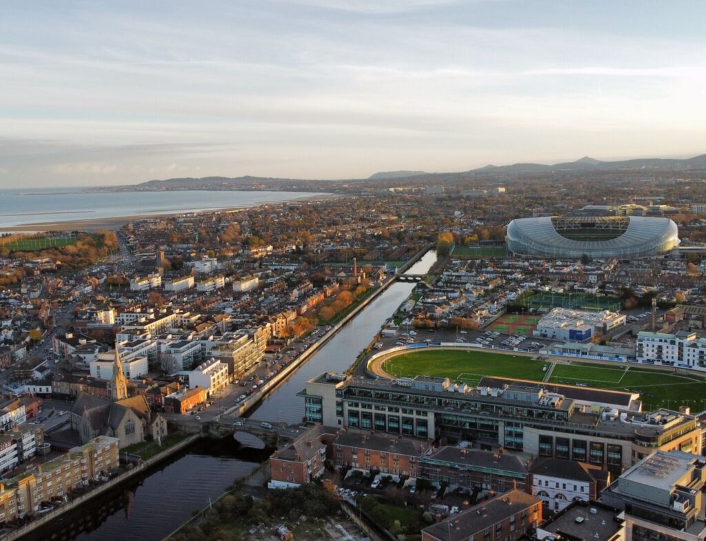 Aerial view of Dublin cityscape with Aviva Stadium, River Dodder, and coastline in the background at sunset.