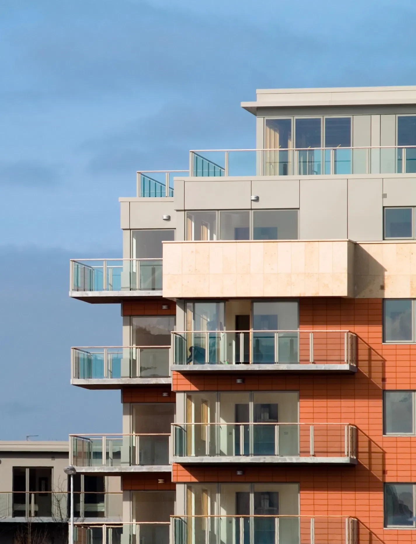 Modern apartment building with glass balconies set against a blue sky, showcasing contemporary architecture.
