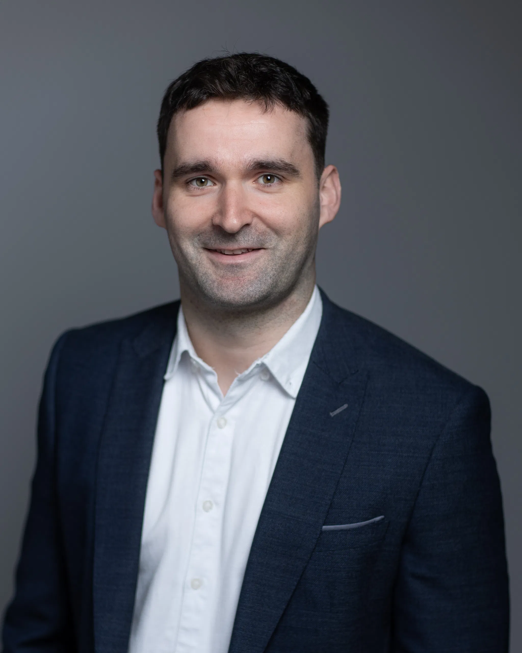 Professional man in a suit with a neutral background, smiling confidently at the camera.