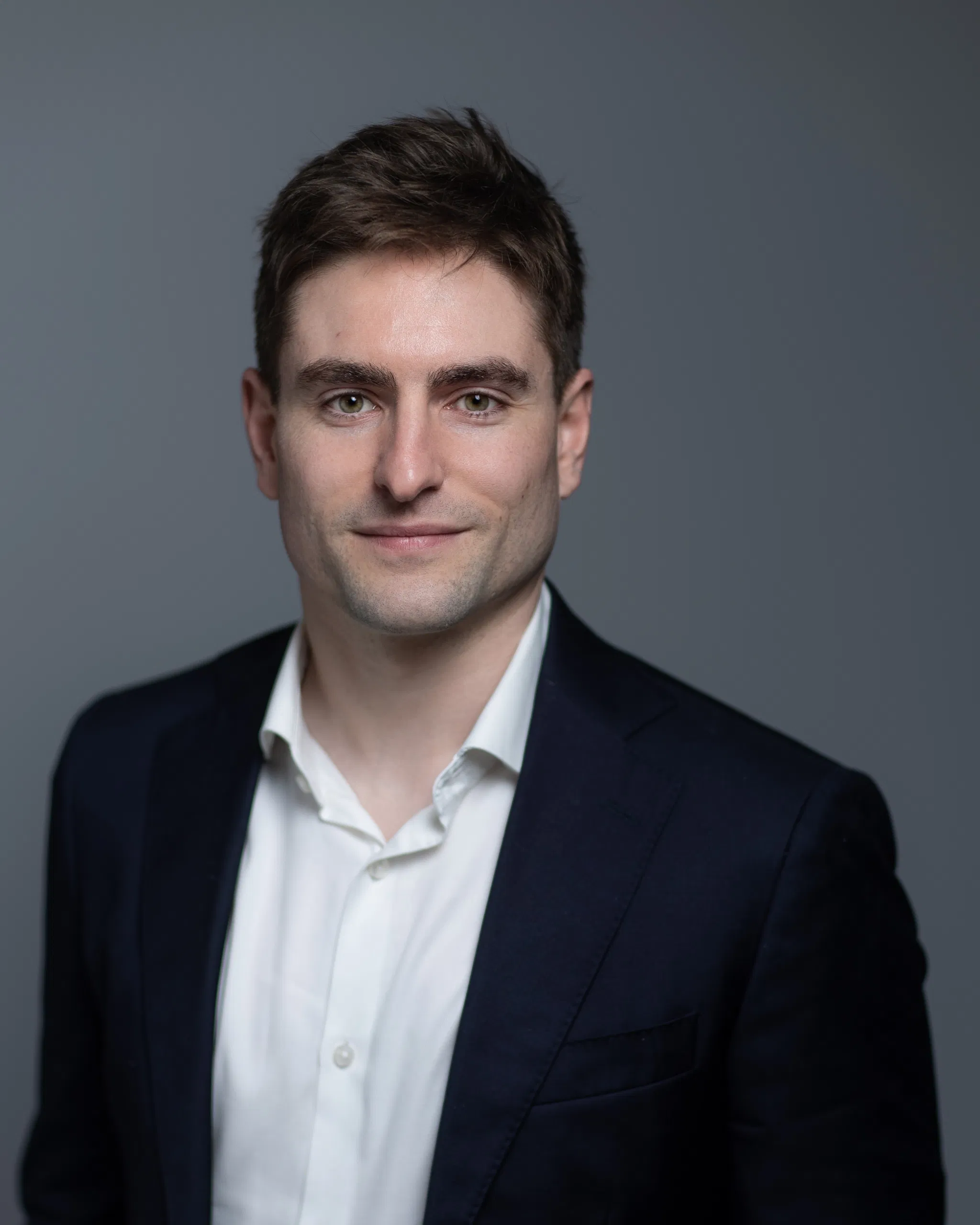 Professional man in suit, white shirt, smiling, neutral background.