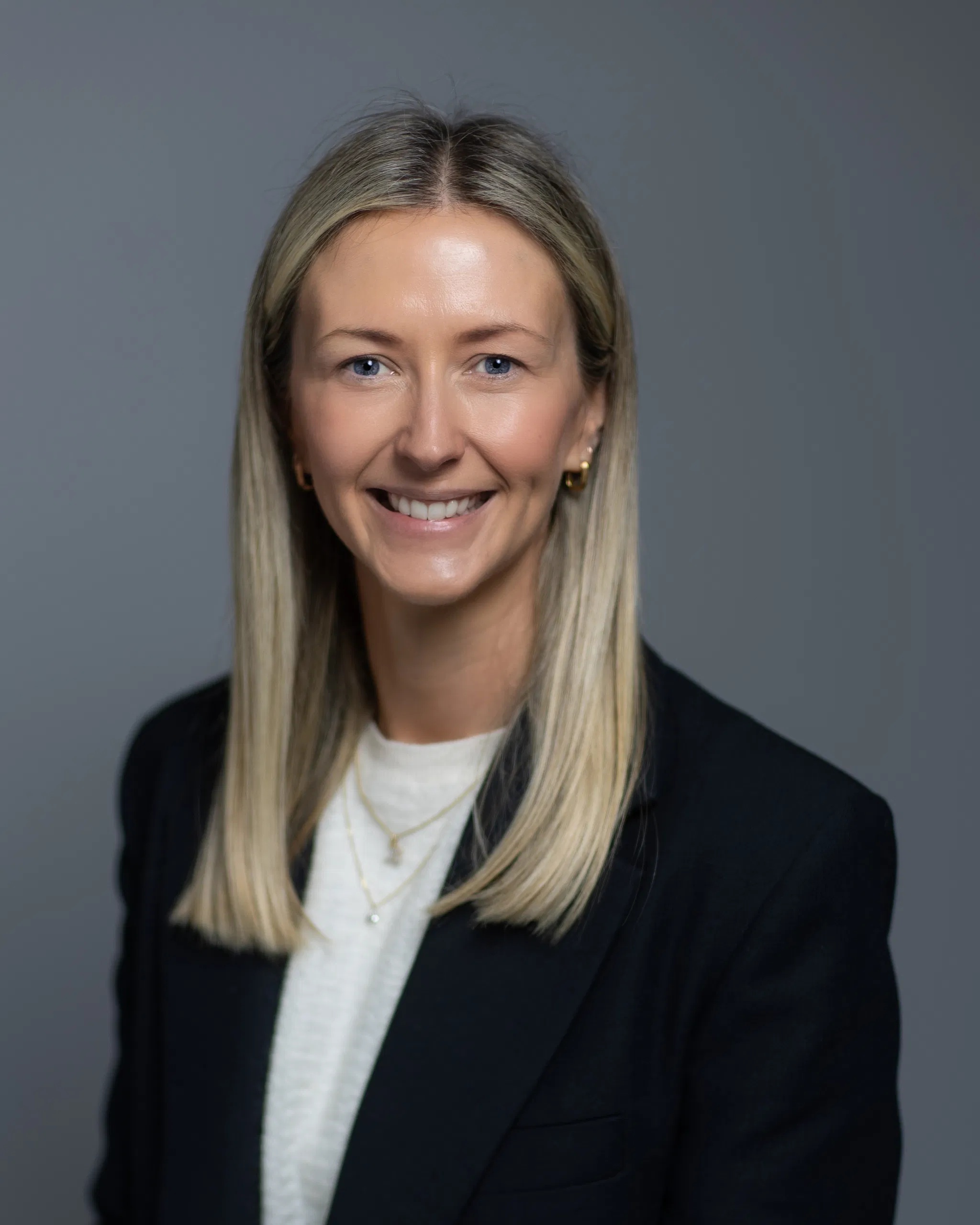 Portrait of a smiling woman in a blazer and white top, on a gray background.