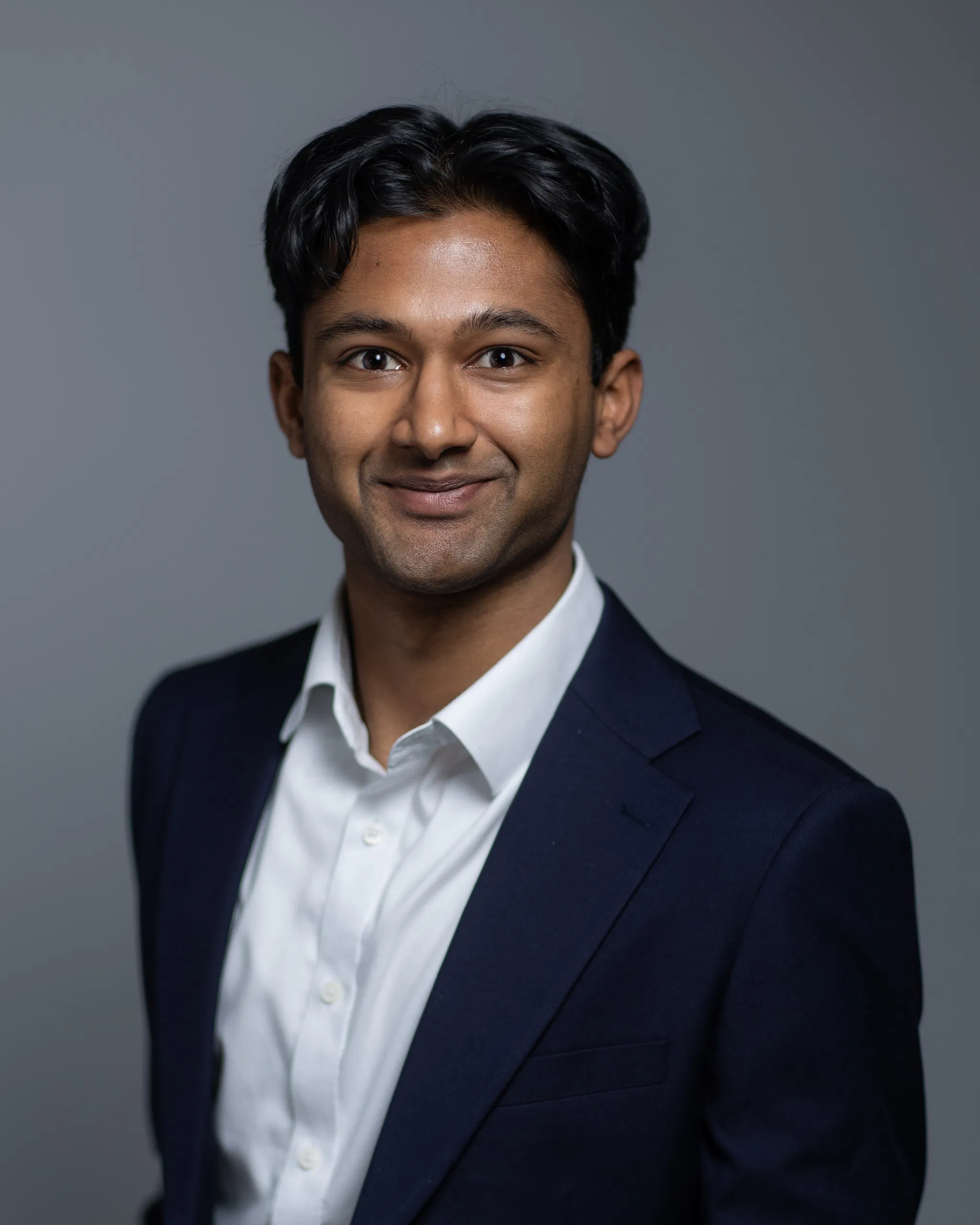 Professional portrait of a person in a suit with a neutral background, smiling confidently.