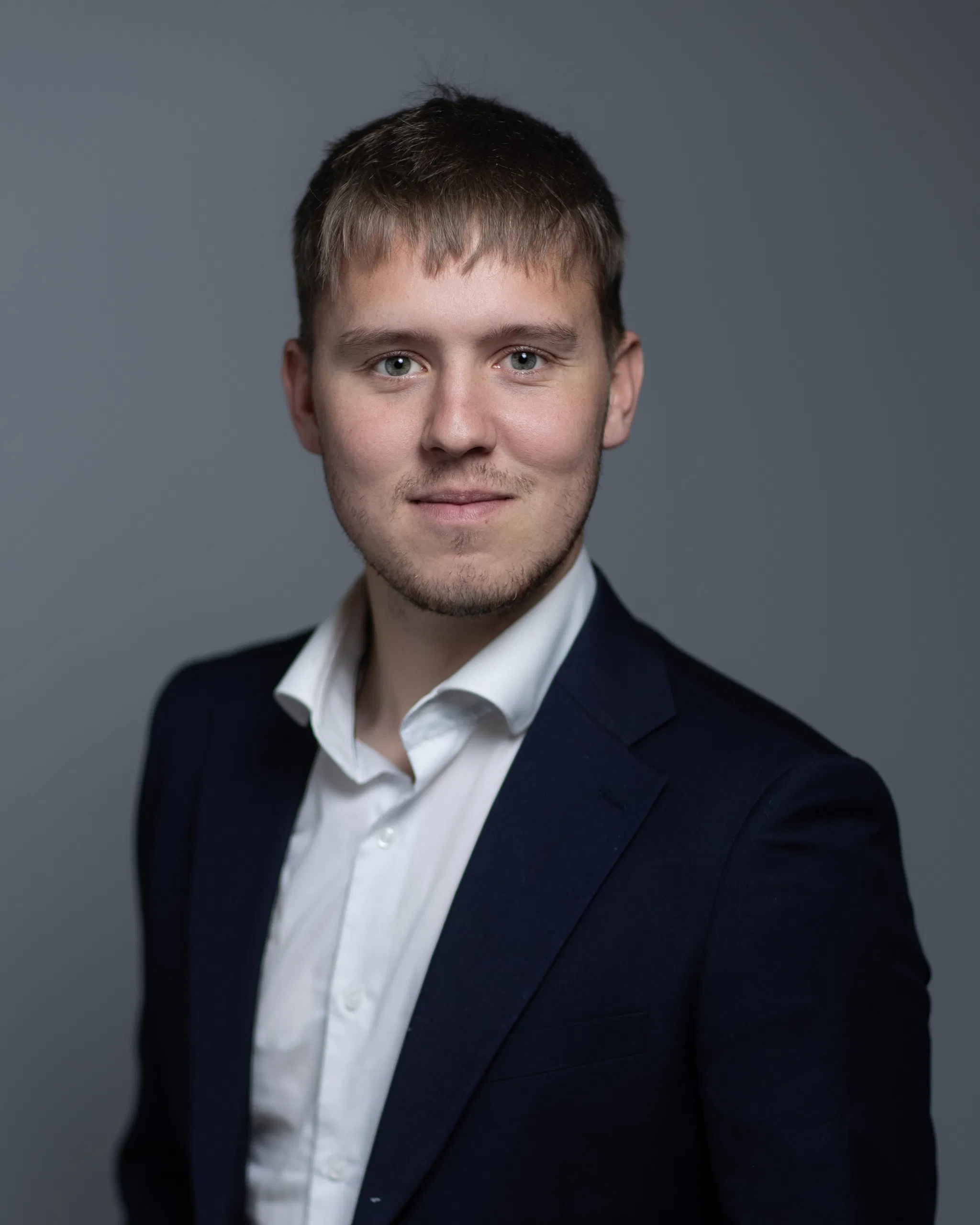 Professional man in a suit with a confident expression, posing against a neutral gray background.