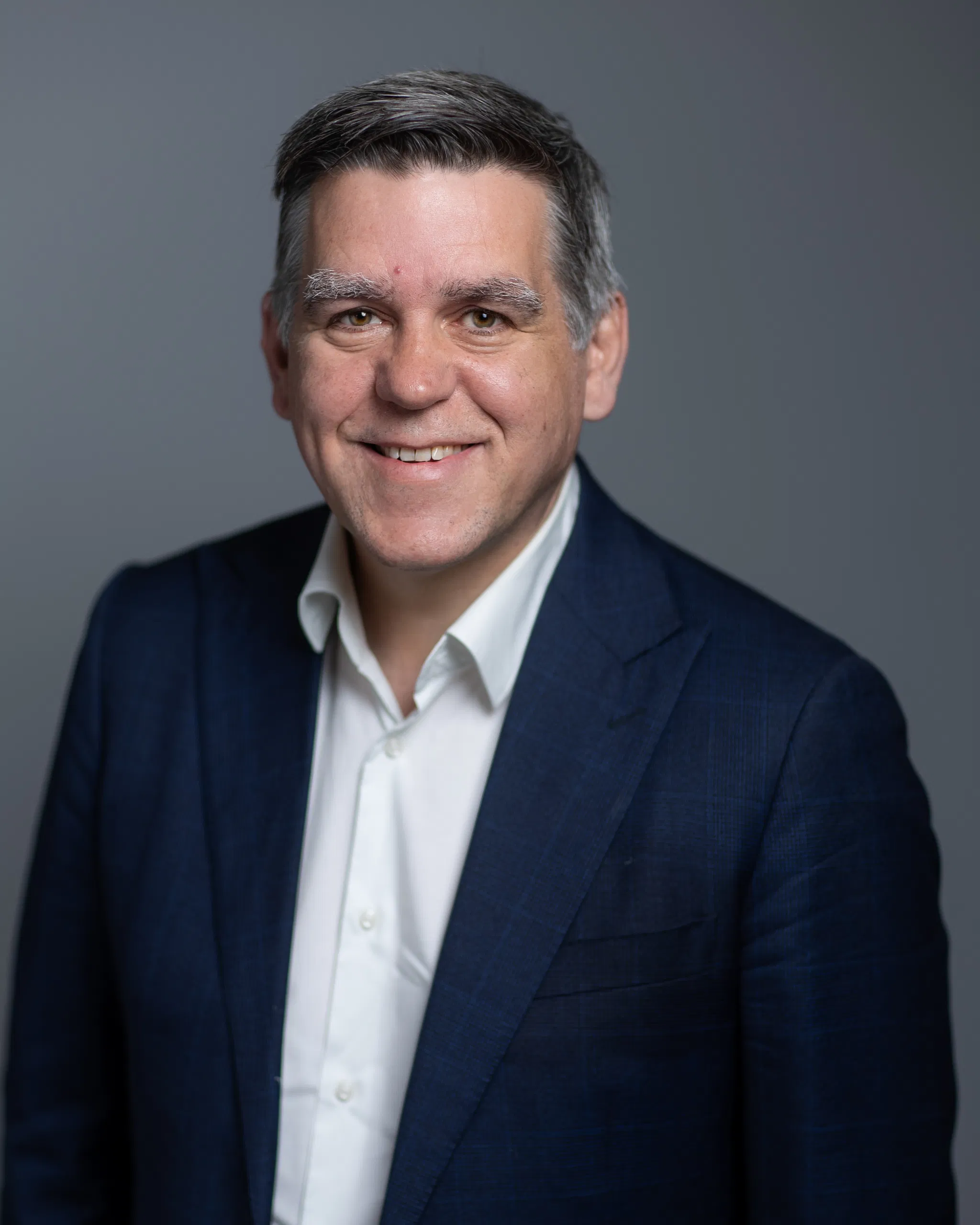 Smiling man in a blue suit and white shirt against a gray background.